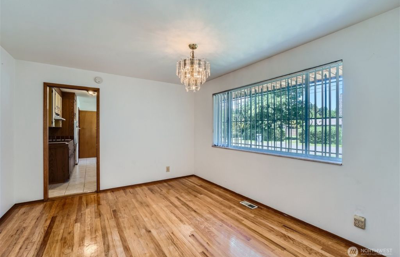 An empty living room with hardwood floors and a large window.