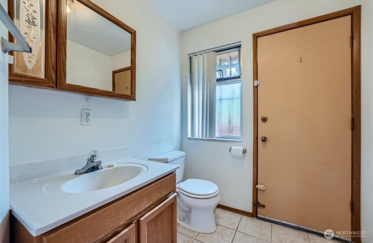 A bathroom with a sink , toilet , mirror and door.