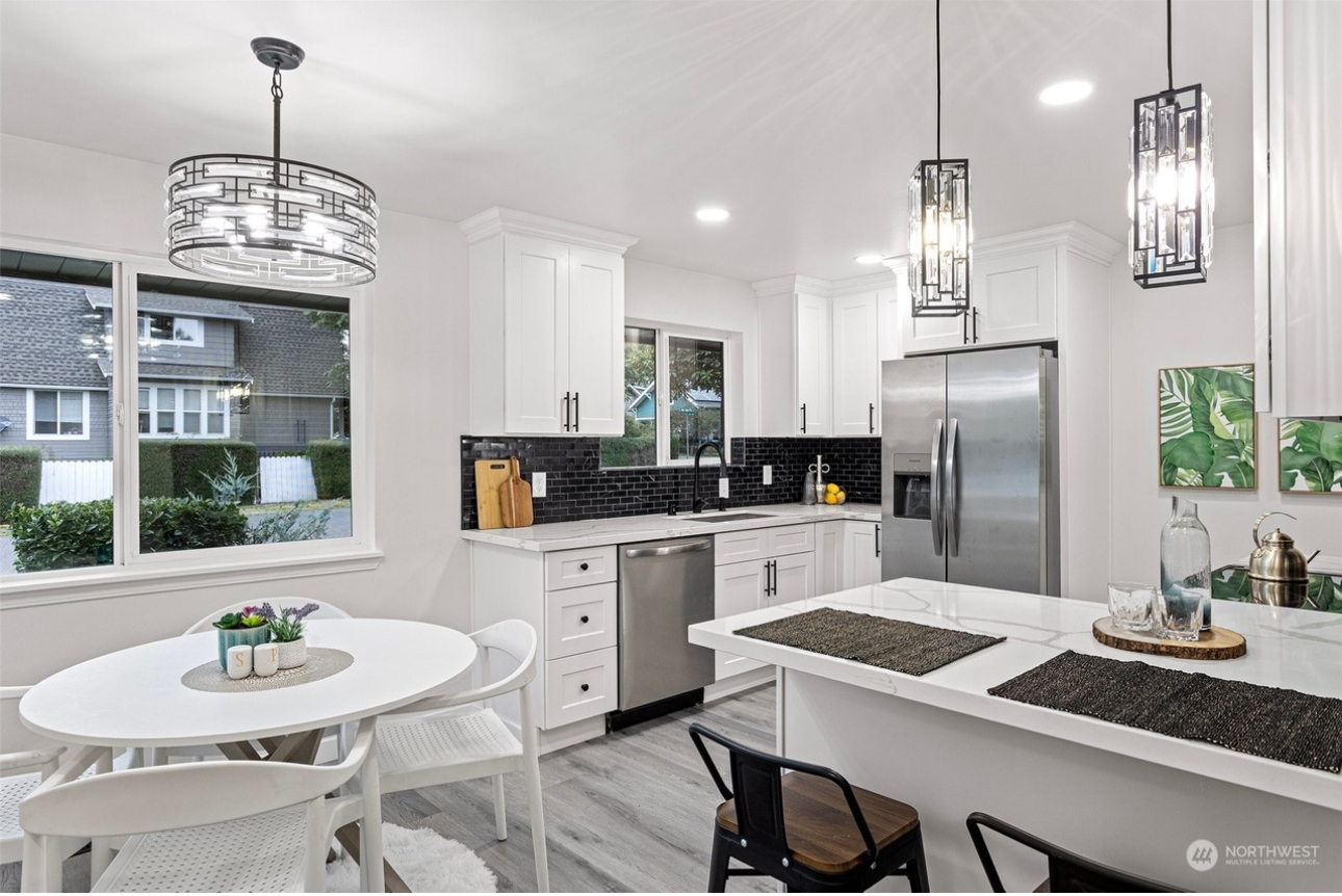 A kitchen with white cabinets , stainless steel appliances , a table and chairs.