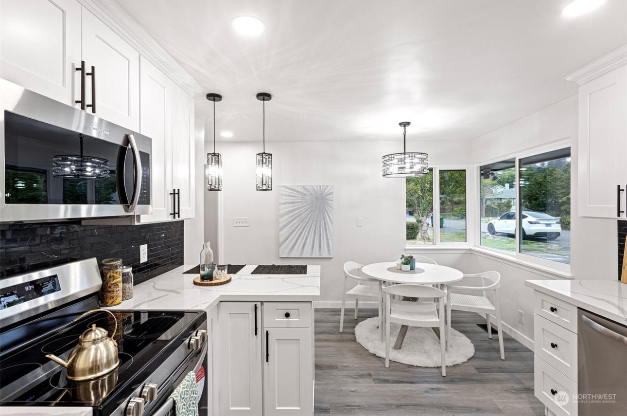 A kitchen with white cabinets and stainless steel appliances and a dining room with a table and chairs.