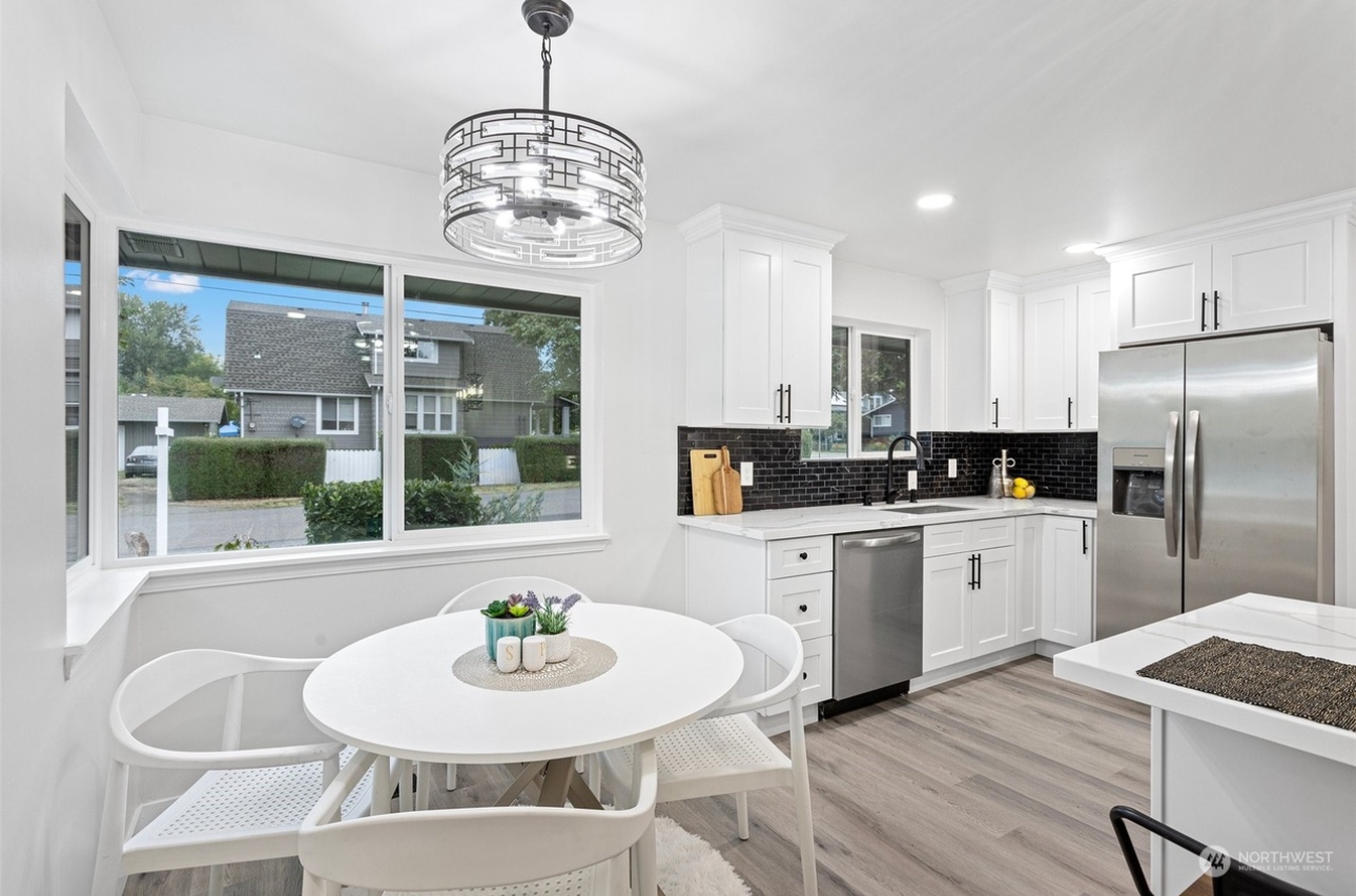 A kitchen with white cabinets , stainless steel appliances , a round table and chairs.