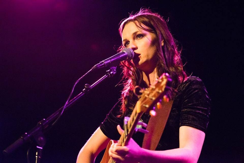 A woman is singing into a microphone while playing a guitar.
