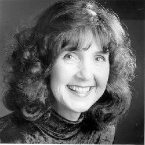 A woman with curly hair is smiling in a black and white photo.