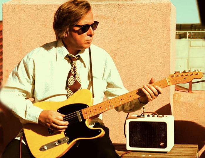 A man wearing sunglasses is playing a guitar