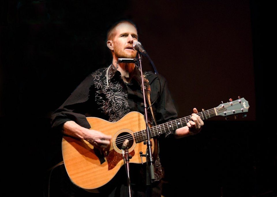 A man singing into a microphone while holding a guitar