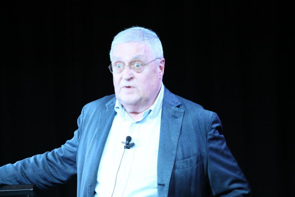 A man in a suit and glasses is standing in front of a microphone.
