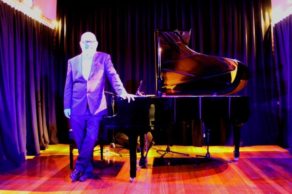 A man in a suit is standing next to a piano on a stage.