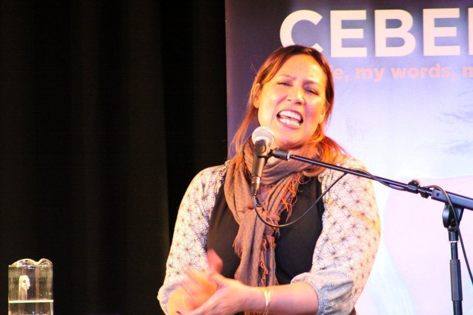 A woman singing into a microphone in front of a banner that says cebel