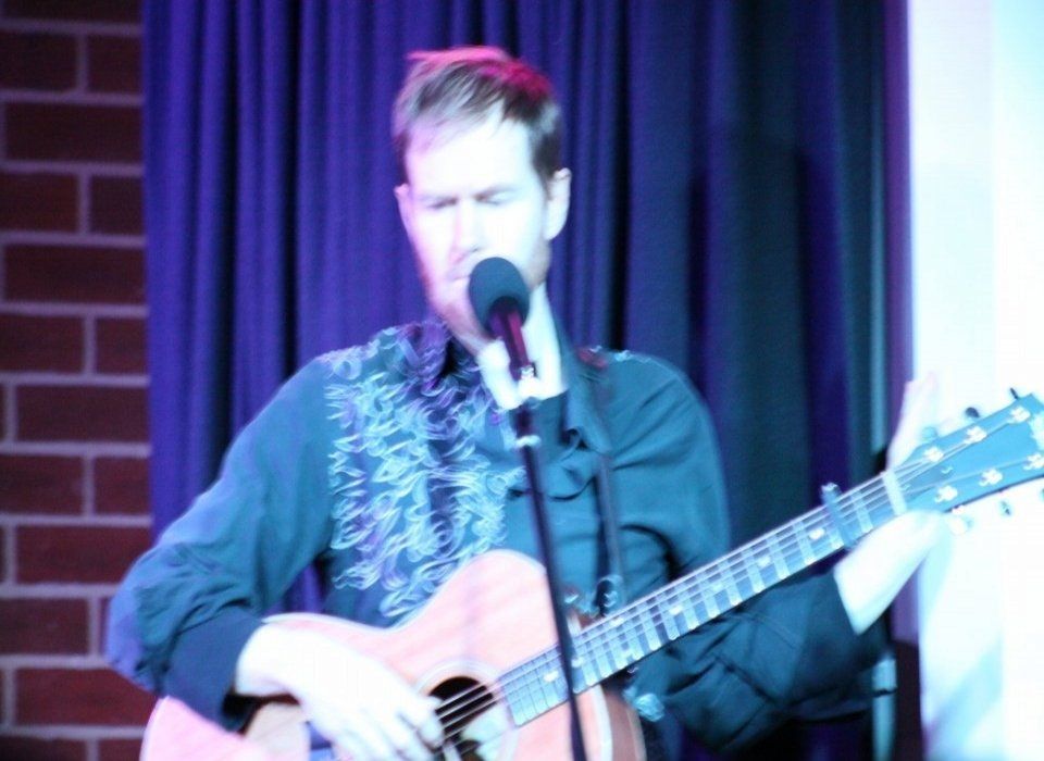 A man singing into a microphone while playing a guitar