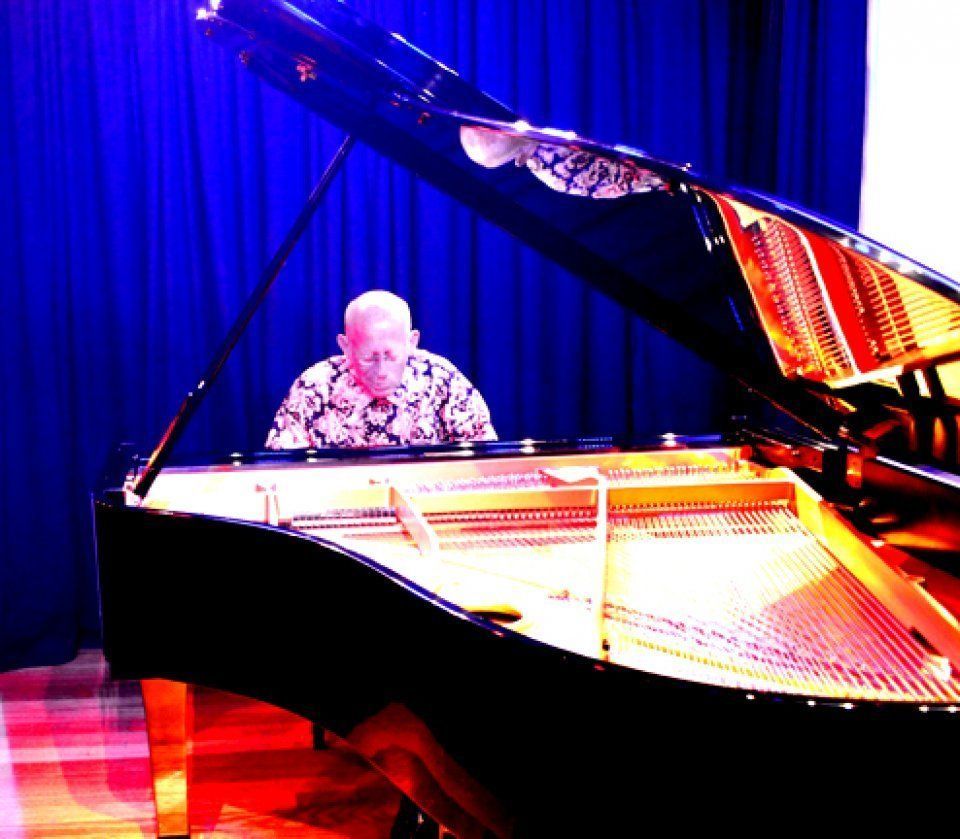A man is playing a grand piano in front of a blue curtain