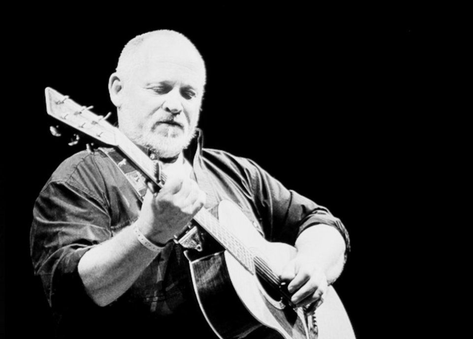 A man with a beard is playing a guitar in a black and white photo.