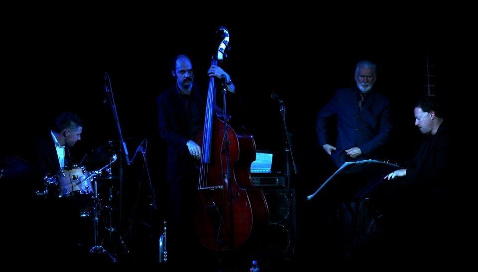 A group of men are playing instruments on a stage in a dark room.
