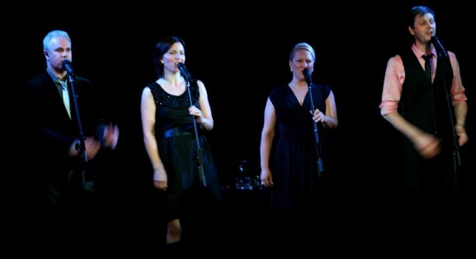 A group of people are singing into microphones on a stage.