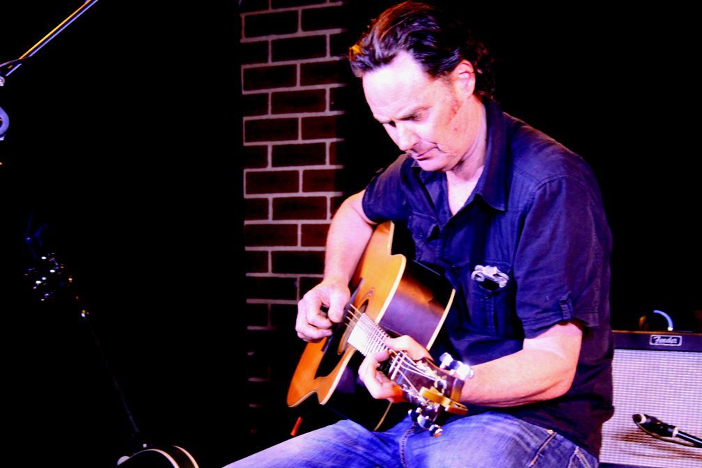A man is playing an acoustic guitar on a stage.