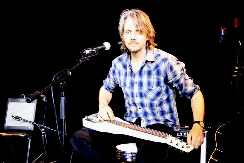 A man in a plaid shirt is playing a guitar in front of a microphone.