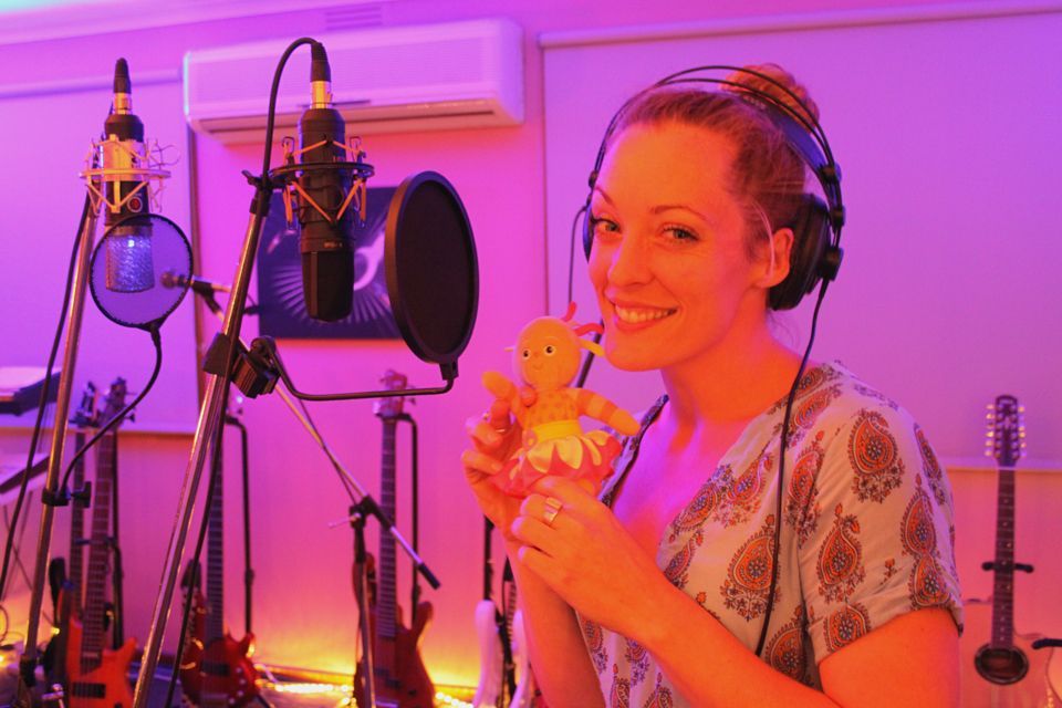 A woman is holding a stuffed animal in front of a microphone in a recording studio.