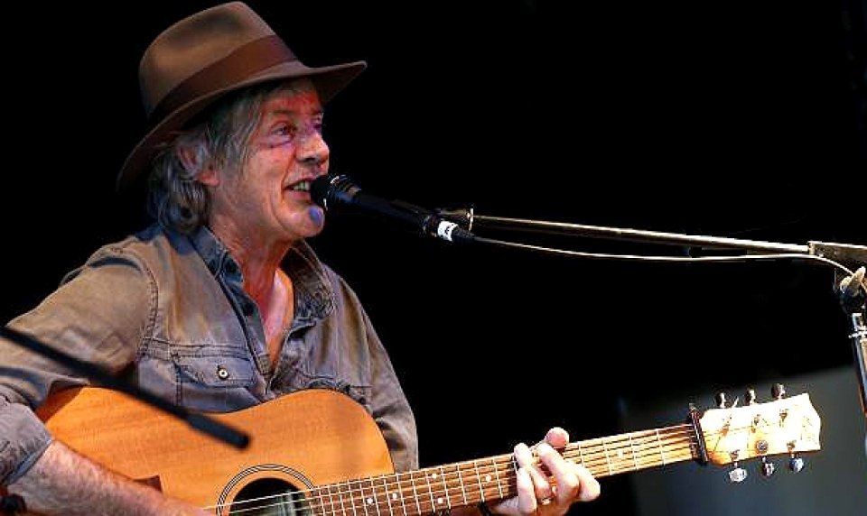 A man in a hat is playing an acoustic guitar and singing into a microphone.