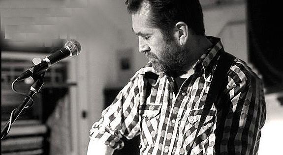 A man in a plaid shirt is singing into a microphone.