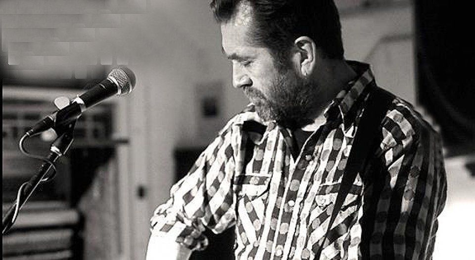 A man in a plaid shirt is singing into a microphone.