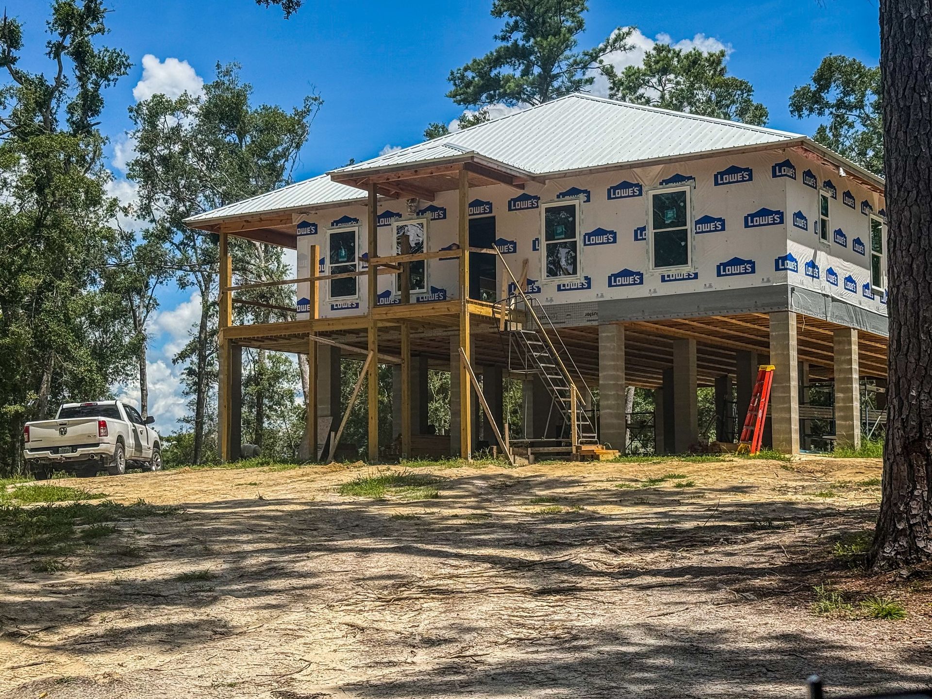 Elevated house under construction in a wooded area, with white wrap and a truck.
