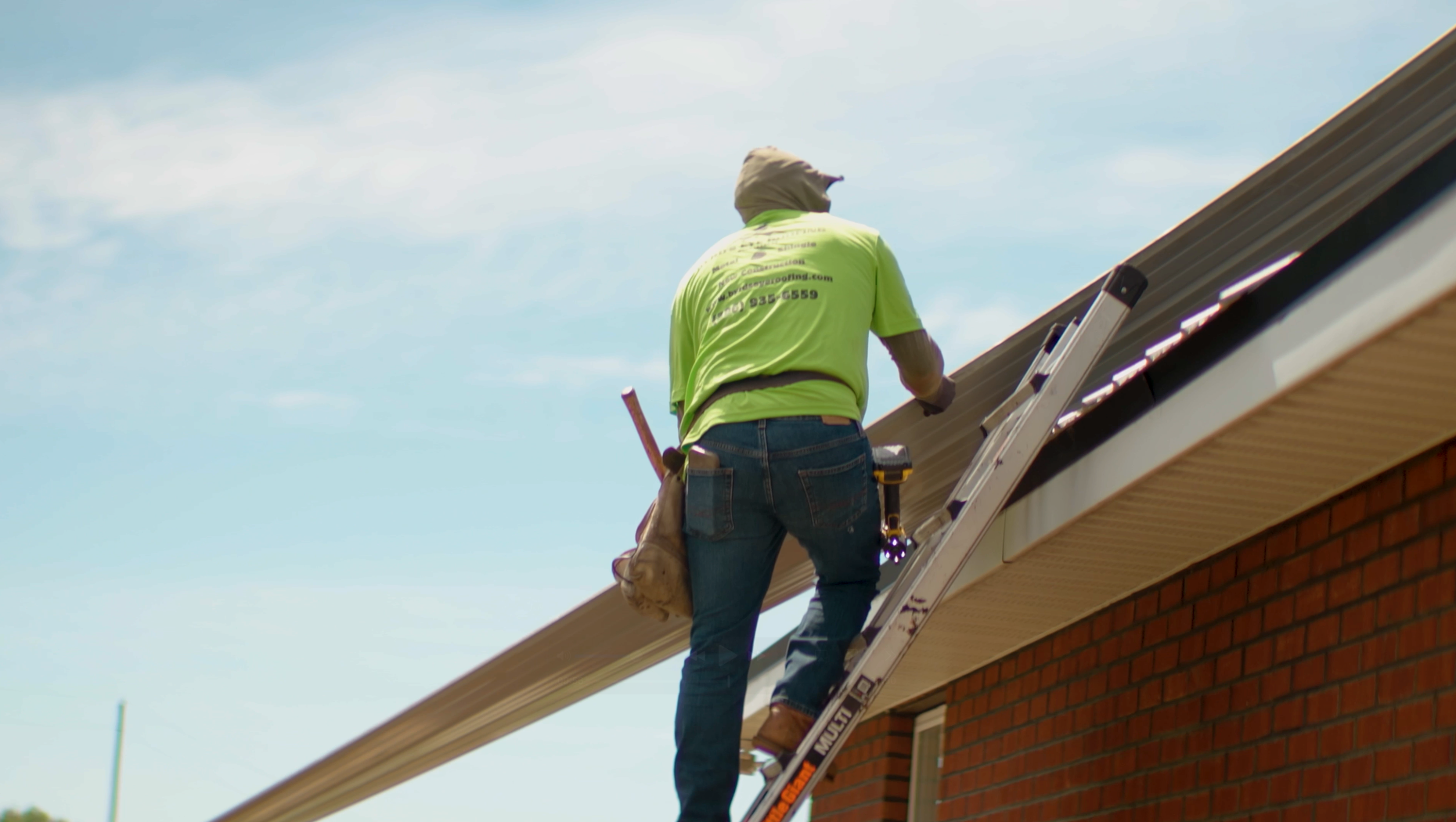 Construction worker on a ladder, installing soffit on a brick building under a blue sky.