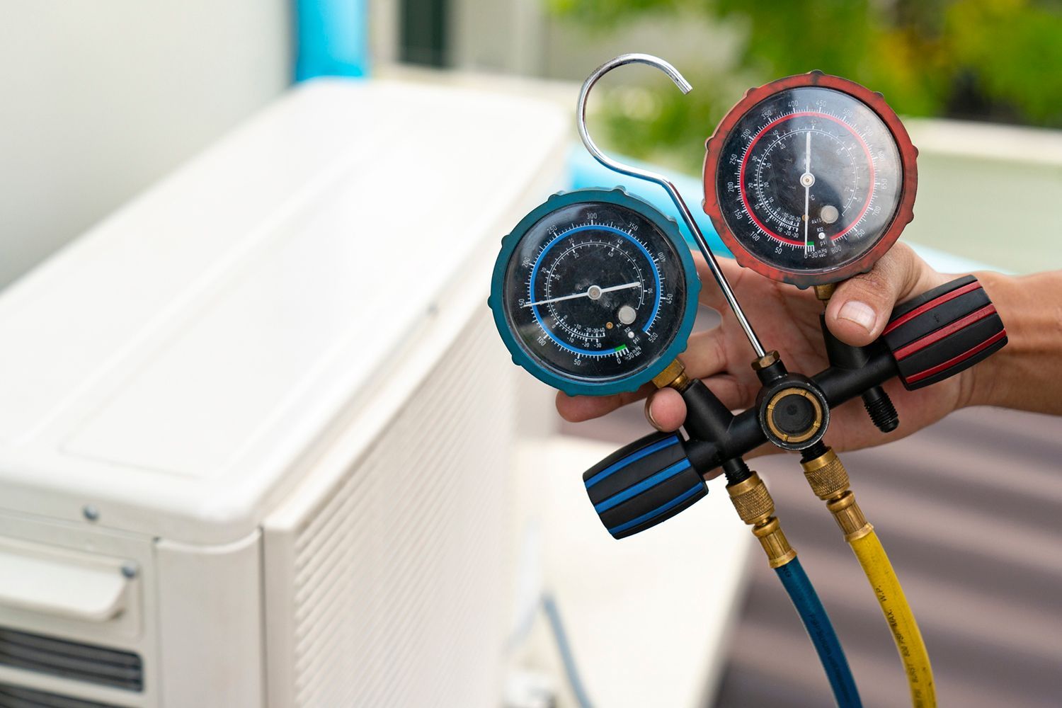 Hand holding gauges connected to an air conditioning unit, checking pressure.