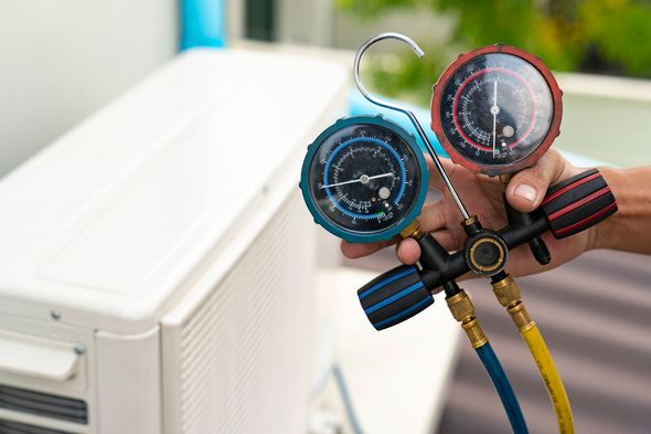 Hand holding gauges connected to an air conditioning unit, checking pressure.