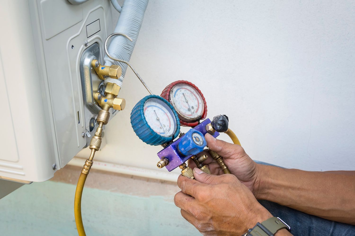 Hands attaching gauges to an outdoor AC unit, likely for repair or maintenance.