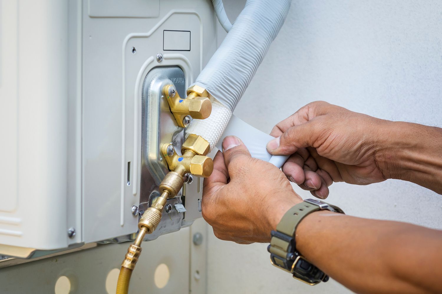A person installing an air conditioner unit, connecting refrigerant lines.