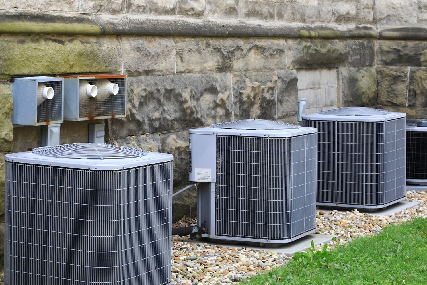 Air conditioning units lined up against a stone building.