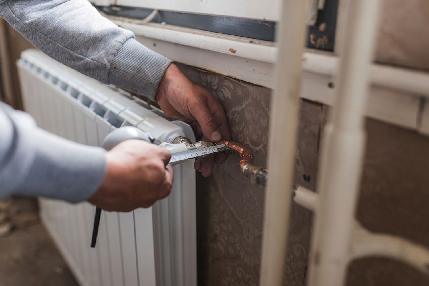Person working on a radiator, using a tool to adjust copper piping near a window.
