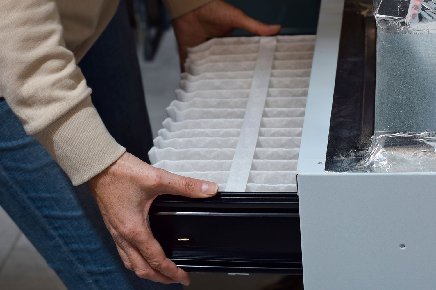 Person replacing an air filter in a furnace, showing the filter and the unit's opening.