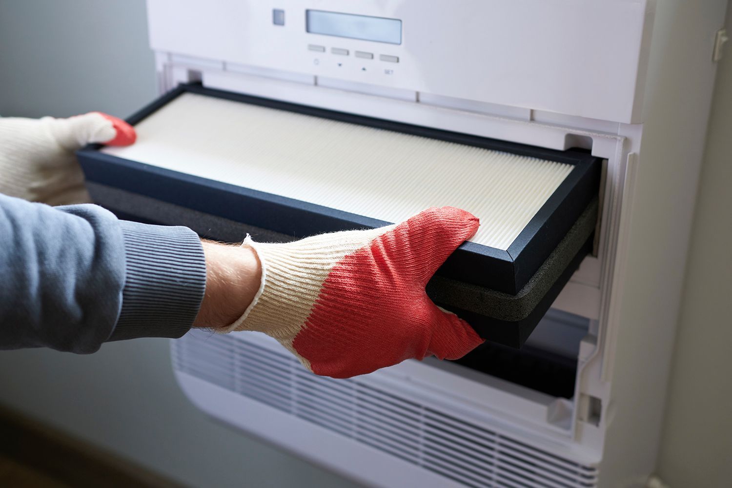 Hands in gloves removing an air filter from a white air purifier.