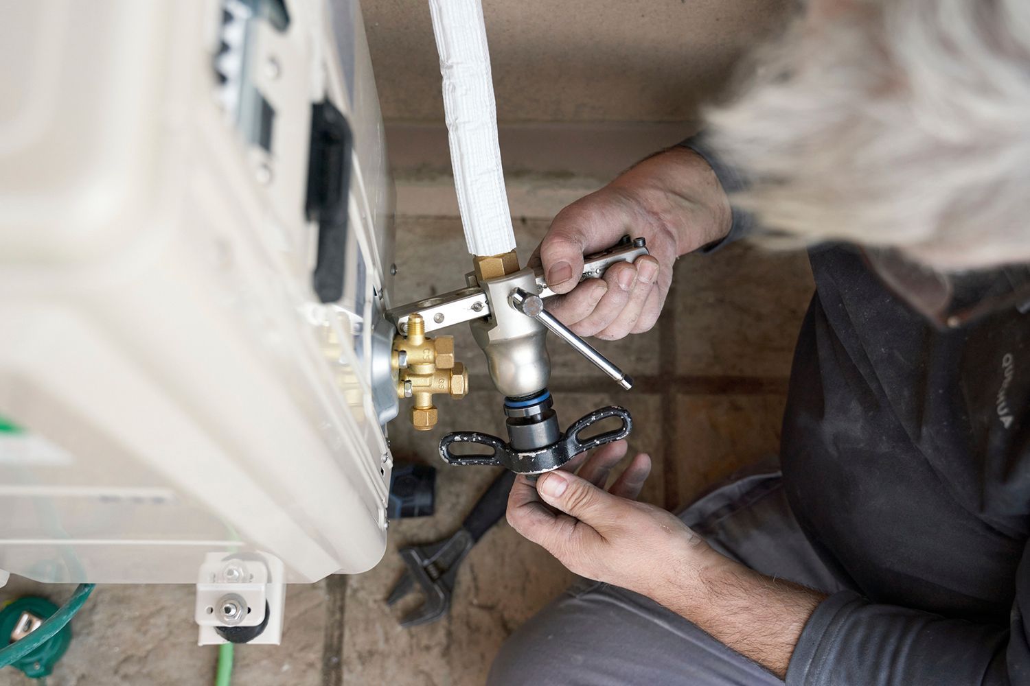 Person installing plumbing under a sink, using a wrench and connecting pipes.