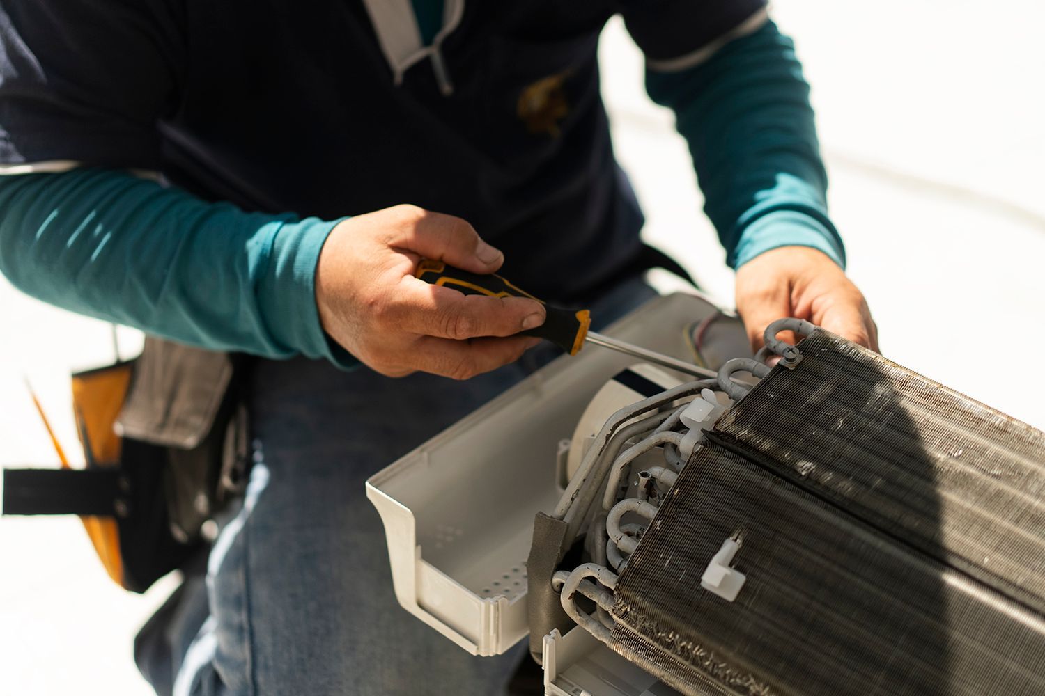 A person in work attire using a screwdriver on HVAC components outside.