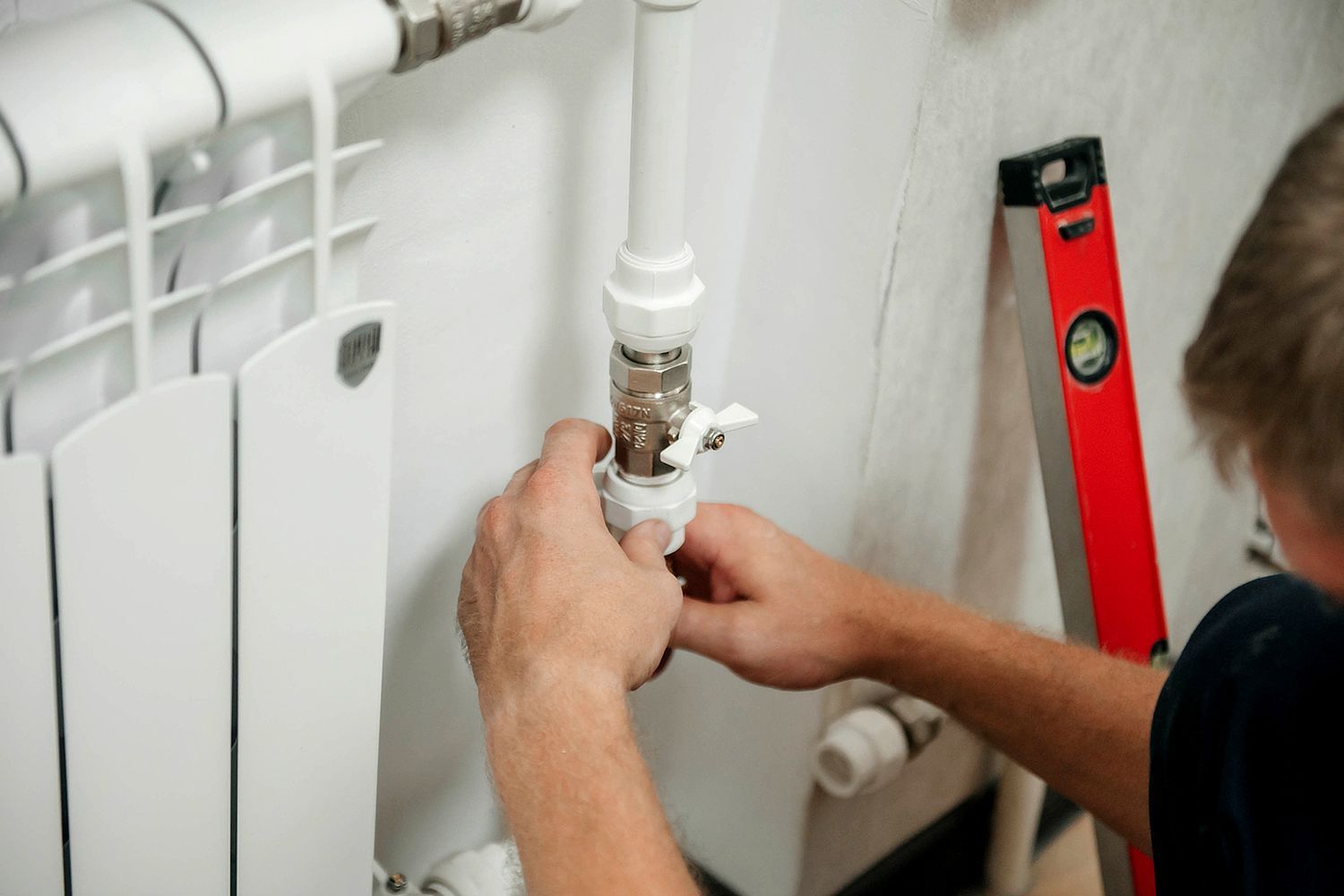 A person repairing a white radiator, using tools next to a level on a white wall.