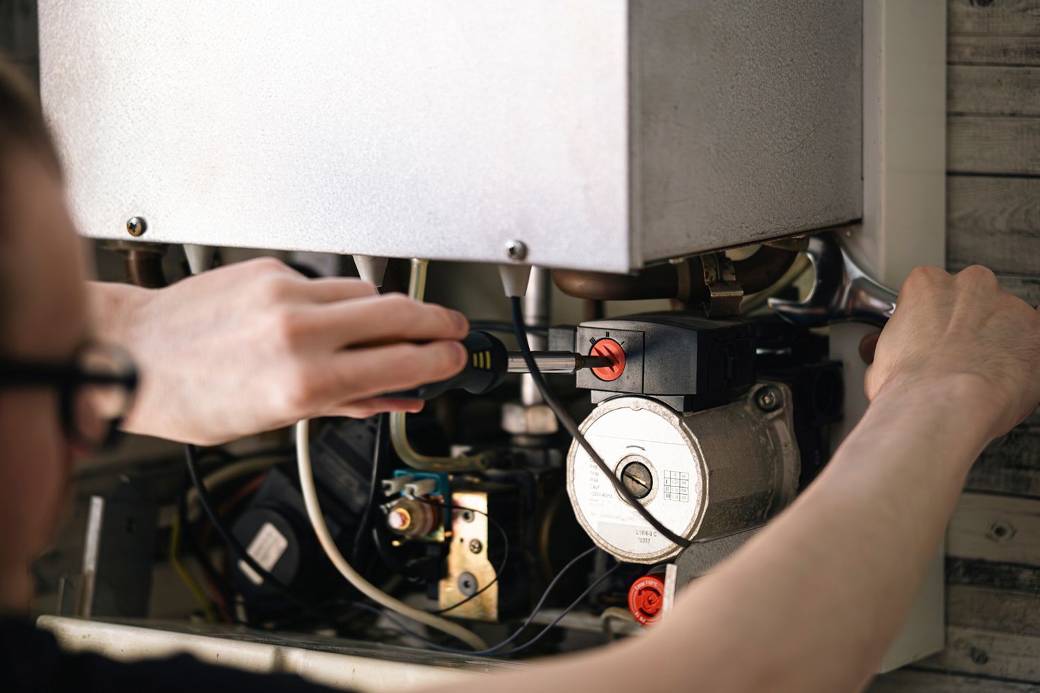 Person using tools to repair a furnace in a home.