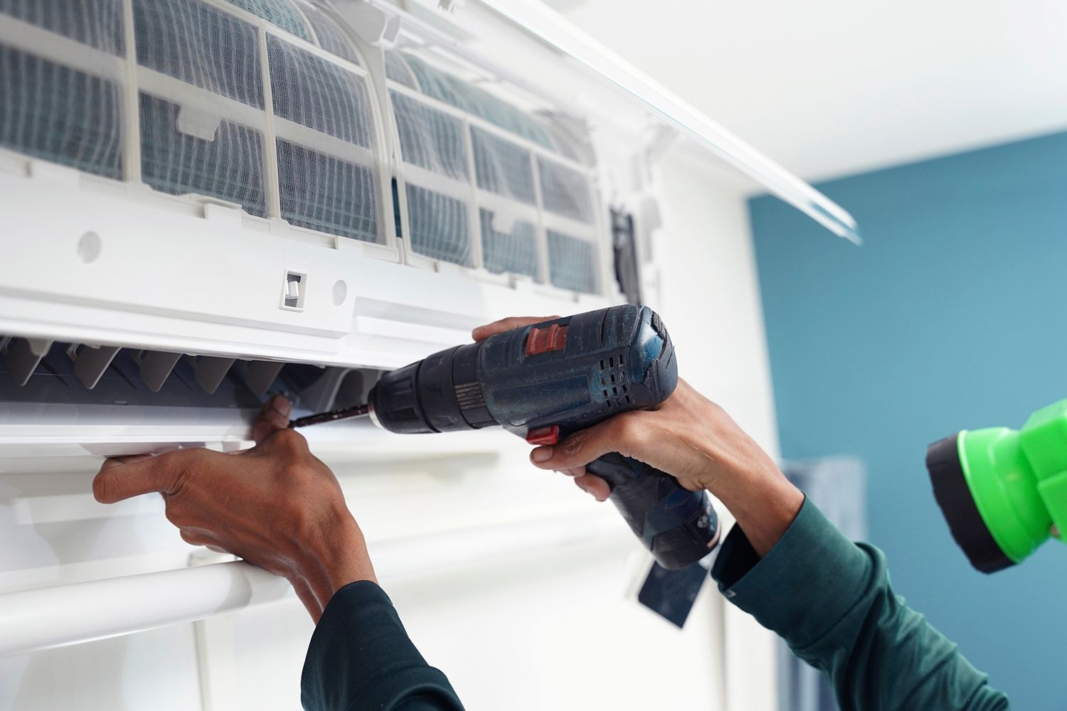 Person using a drill to work on an air conditioning unit, indoors.