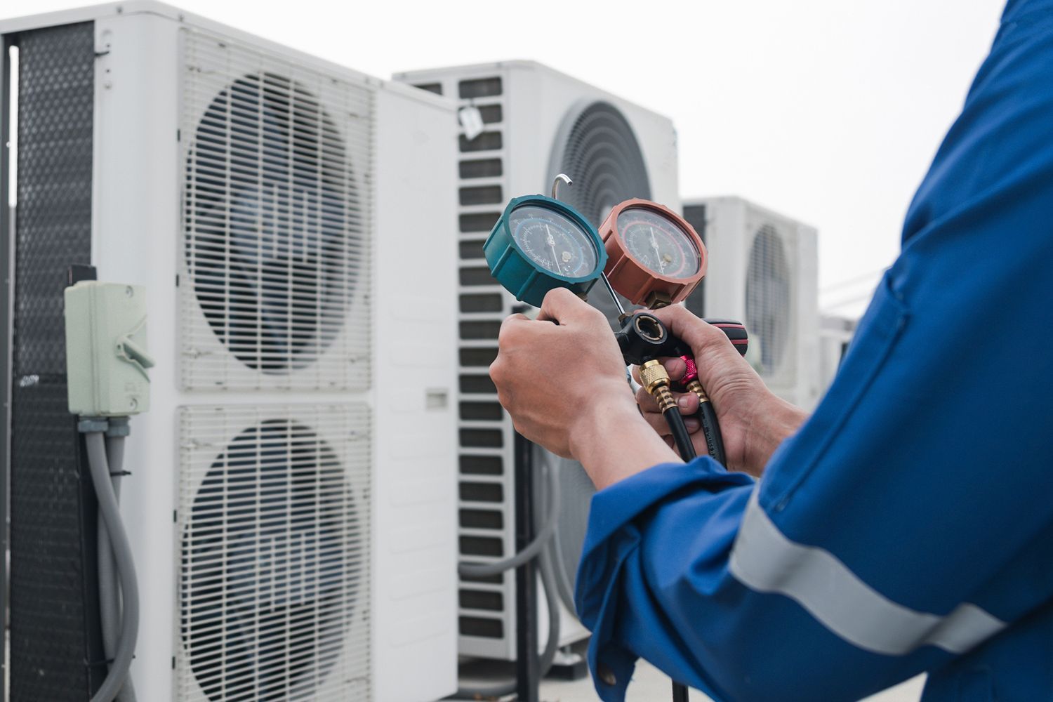 HVAC technician checks gauges on an AC unit, outdoors.