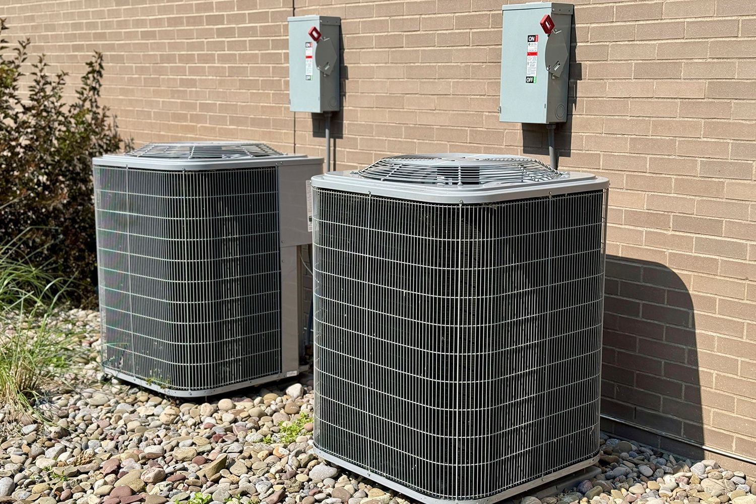 Two outdoor air conditioning units next to a brick building.