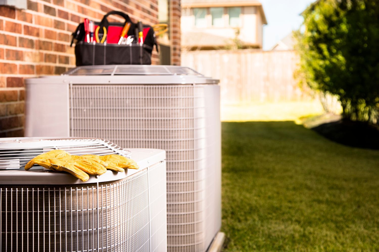 Two AC units in a yard with a toolbox, work gloves, and a brick wall.