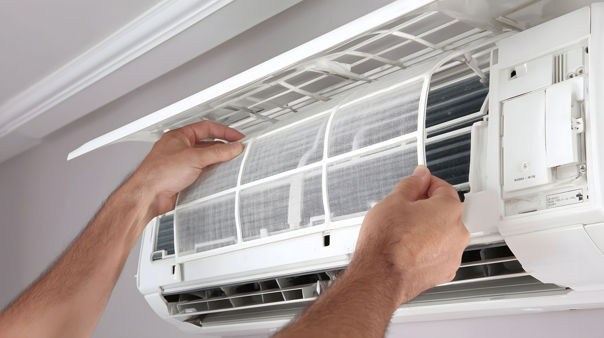 Person removing air filter from a white wall-mounted air conditioner.