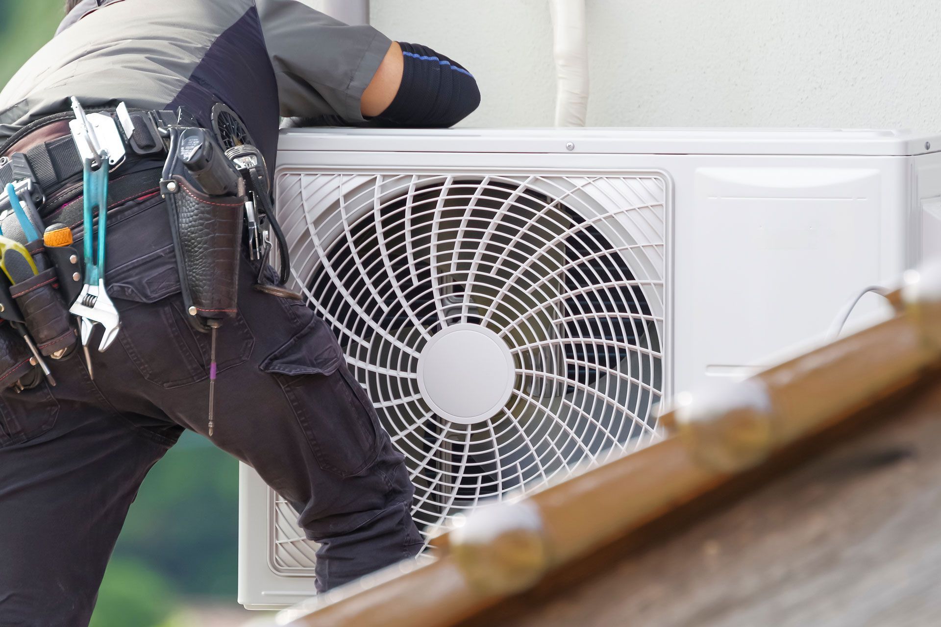 HVAC technician working on an outdoor air conditioning unit; tools and belt visible.