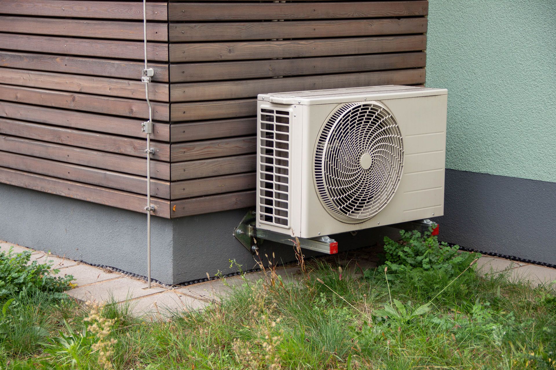Exterior air conditioning unit next to a building with wooden siding, sitting in grass.