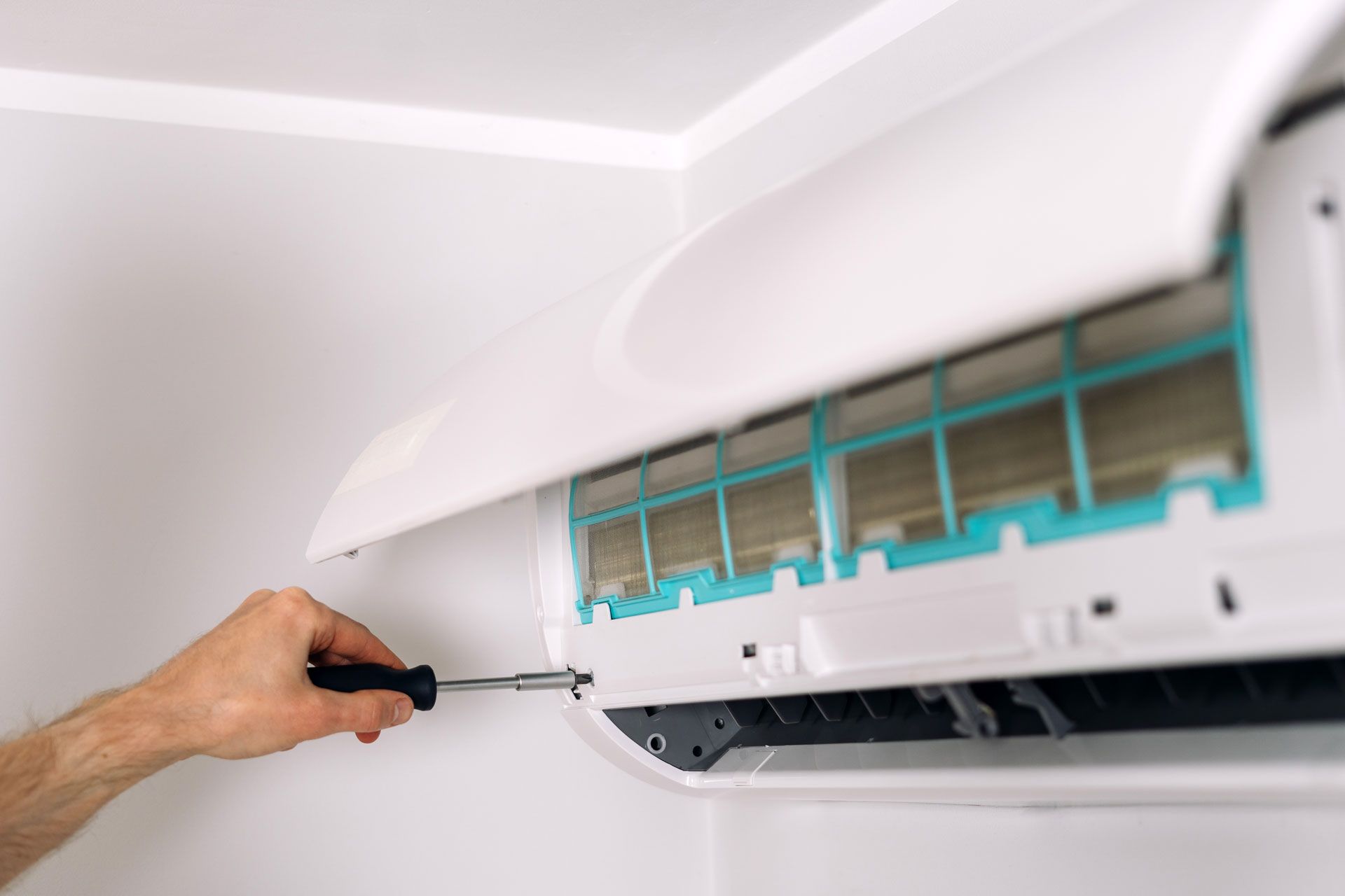 Hand with screwdriver opening a white air conditioner panel, revealing blue filters.