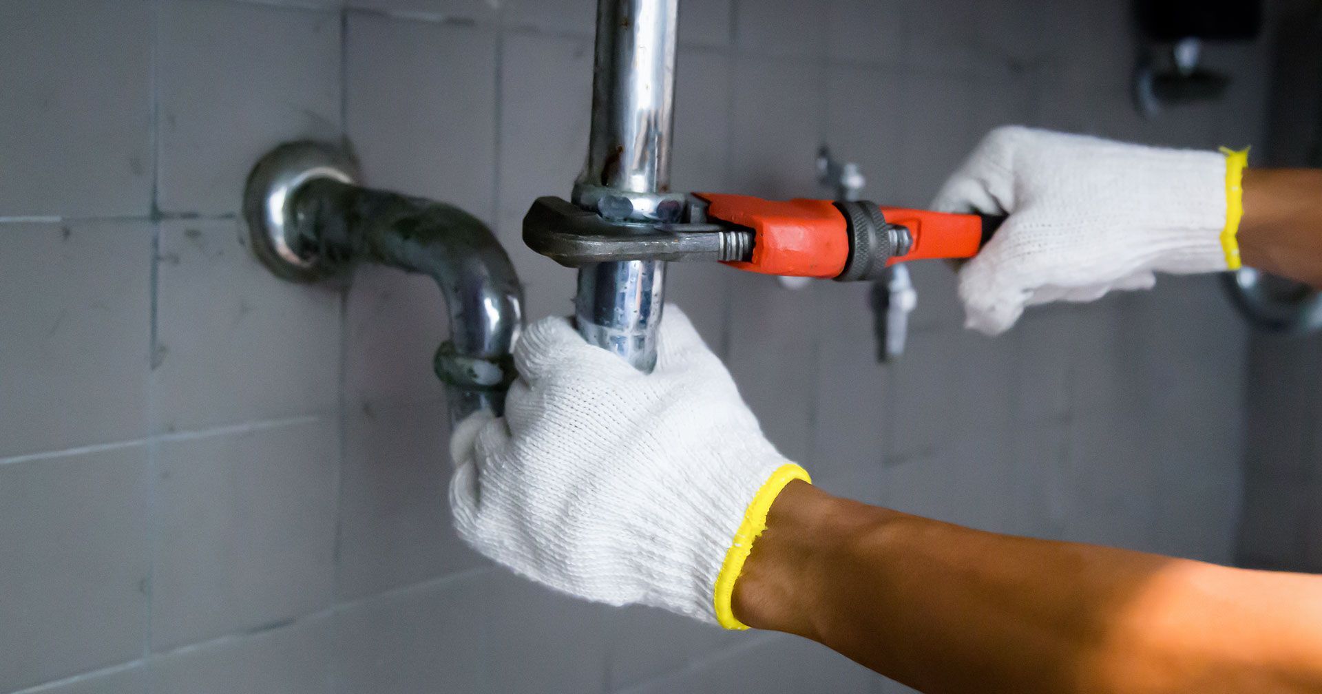 Plumber with a wrench fixing a pipe in a bathroom, wearing gloves. Plumber with a wrench fixing a pipe in a bathroom, wearing gloves.