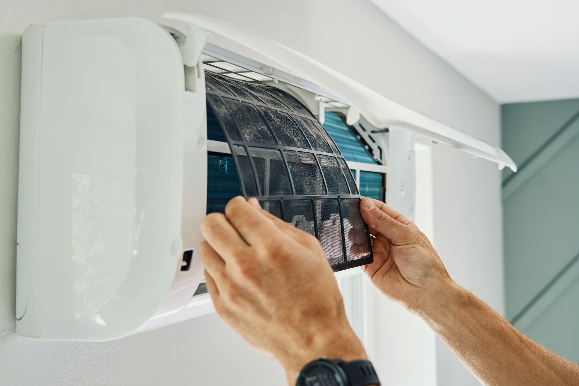 Person removing a dirty air filter from a wall-mounted air conditioner.