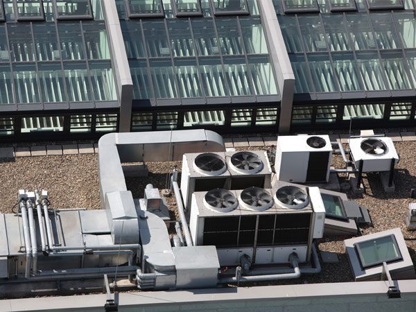Rooftop with HVAC equipment, including fans and ducts, next to a glass roof structure.