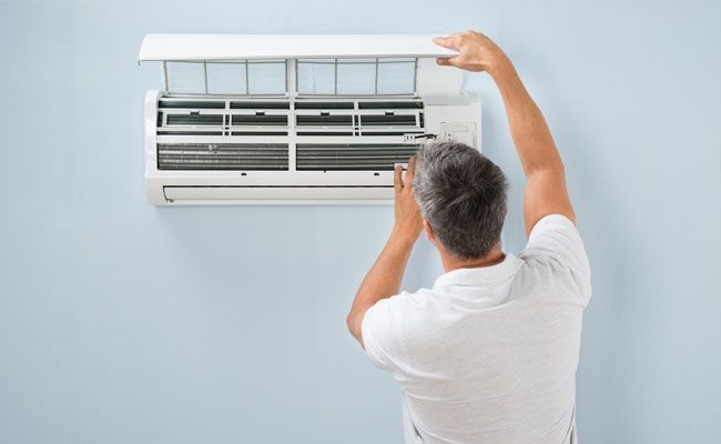 Man in white shirt cleaning an air conditioner filter mounted on a light blue wall.
