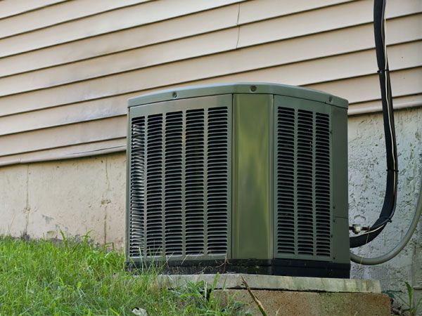 HVAC technician in blue jumpsuit working on an air conditioning unit outside a home.